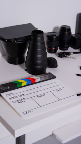 Vertical-Video-Close-Up-Of-Film-Clapperboard-Or-Slate-With-Camera-Lenses-And-Lighting-Accessories-Shooting-Movie-Or-Video-In-Studio